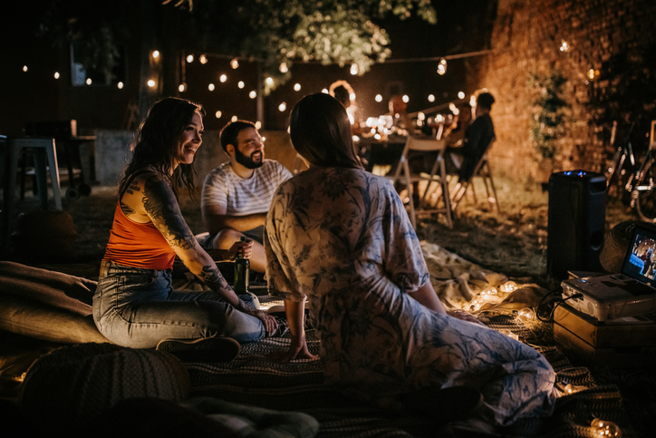 Group of people, men and women together sitting on party in back yard outdoors.