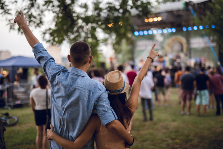 couple holding on to each other with arms raised at an outdoor music concert